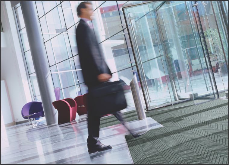 Businessman crossing over a recessed floor mat using Waterhog Eco Elite Roll goods in the entrance of a commercial building