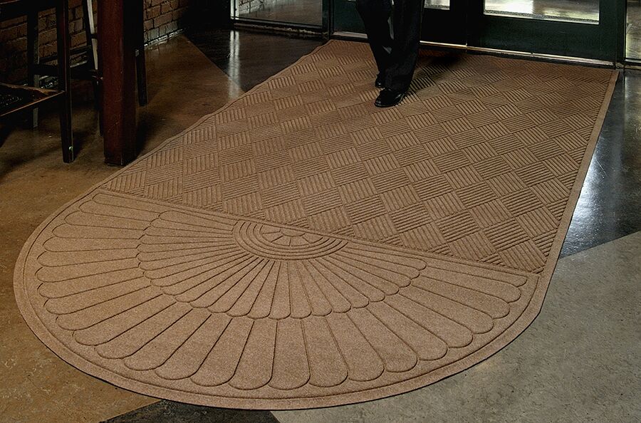 Man walking on a Waterhog Grand Classic Entrance Mat with an oval on one end used as an indoor door mat to a hotel
